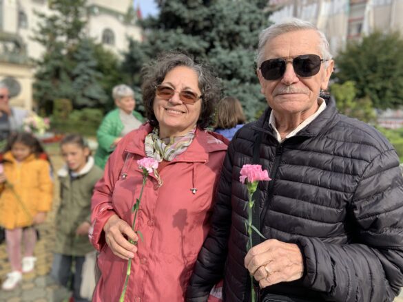 Ziua Internațională a Persoanelor Vârstnice În imagine sunt prezenți un bărbat și o femeie cu câte o floare roz în mână.